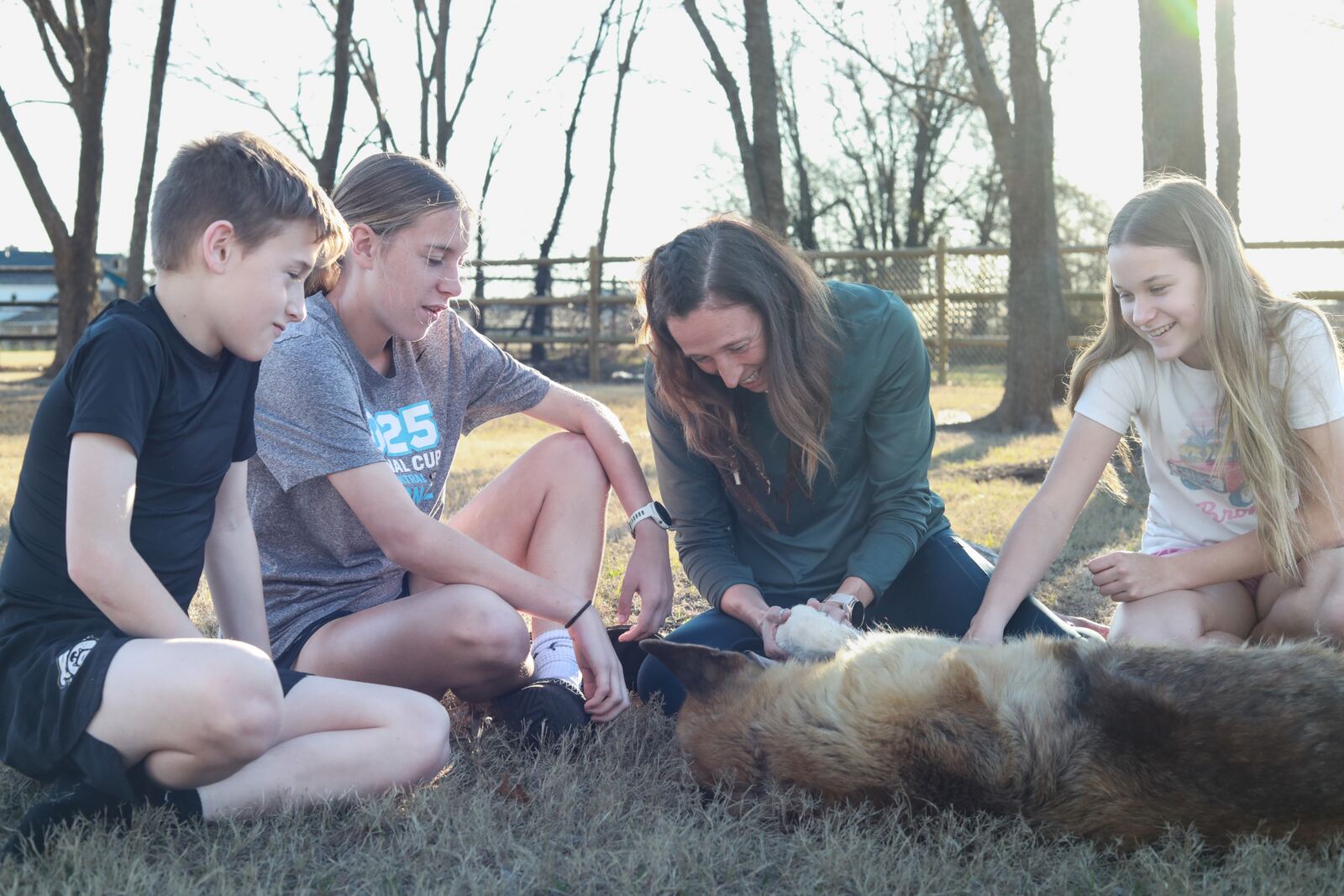 A family gathered around their dog in golden afternoon light.